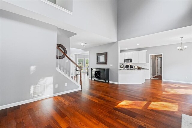 unfurnished living room with visible vents, an inviting chandelier, wood finished floors, baseboards, and stairway
