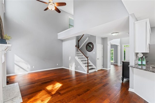 unfurnished living room featuring dark wood-style flooring, a towering ceiling, baseboards, stairway, and a ceiling fan