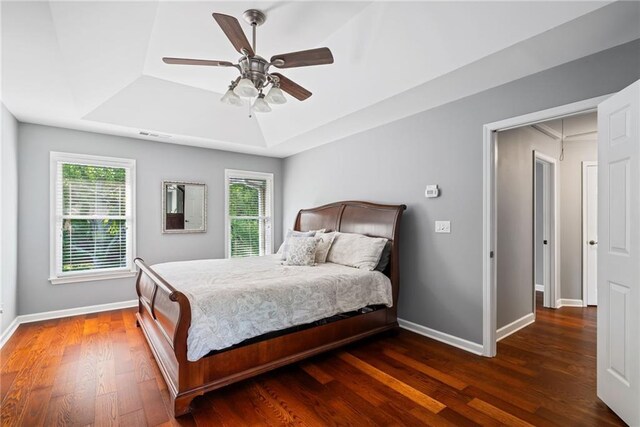 bedroom with ceiling fan, visible vents, wood finished floors, a raised ceiling, and baseboards