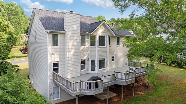 back of property with a shingled roof, a wooden deck, a yard, and a chimney