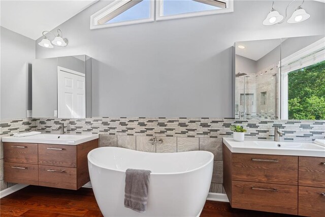 bathroom with a freestanding tub, wood finished floors, two vanities, a sink, and a stall shower
