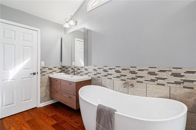 bathroom with wainscoting, vanity, a freestanding tub, tile walls, and wood finished floors