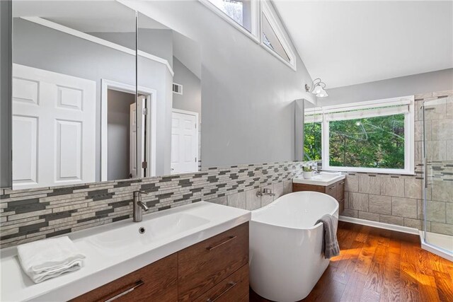 bathroom featuring a freestanding bath, tile walls, wood finished floors, two vanities, and lofted ceiling