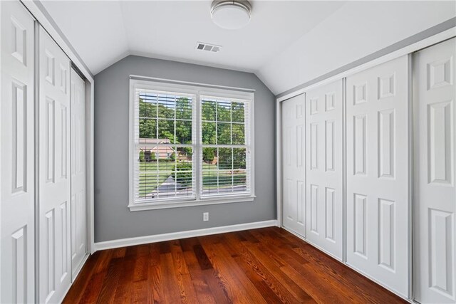 unfurnished bedroom featuring baseboards, vaulted ceiling, dark wood-style floors, and visible vents