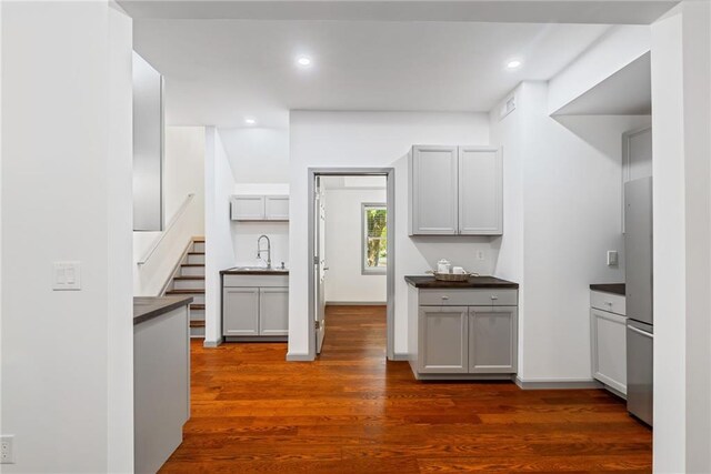 kitchen featuring freestanding refrigerator, dark countertops, dark wood finished floors, and a sink