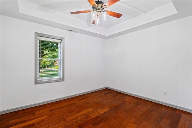 empty room with visible vents, wood finished floors, baseboards, a tray ceiling, and a ceiling fan