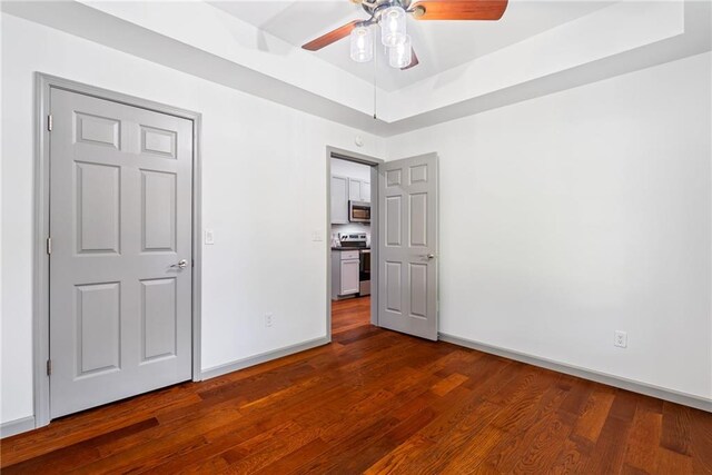 unfurnished bedroom featuring baseboards, dark wood-style flooring, ceiling fan, and a tray ceiling