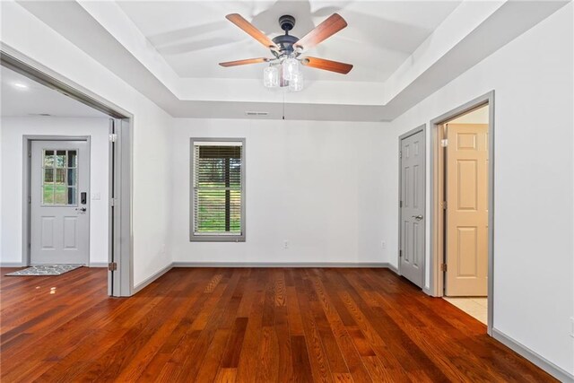 empty room with a ceiling fan, baseboards, a raised ceiling, and hardwood / wood-style floors
