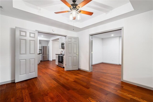 unfurnished living room featuring ceiling fan, dark wood-style flooring, visible vents, a raised ceiling, and baseboards