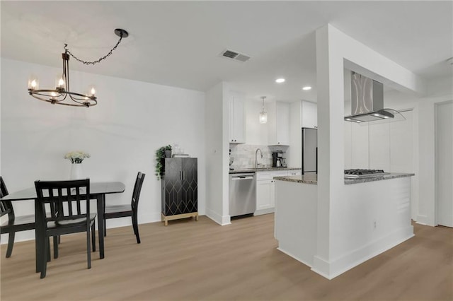 kitchen featuring stainless steel appliances, white cabinets, wall chimney exhaust hood, and light wood-type flooring