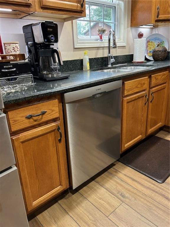 kitchen featuring dark stone countertops, sink, light hardwood / wood-style flooring, and stainless steel dishwasher