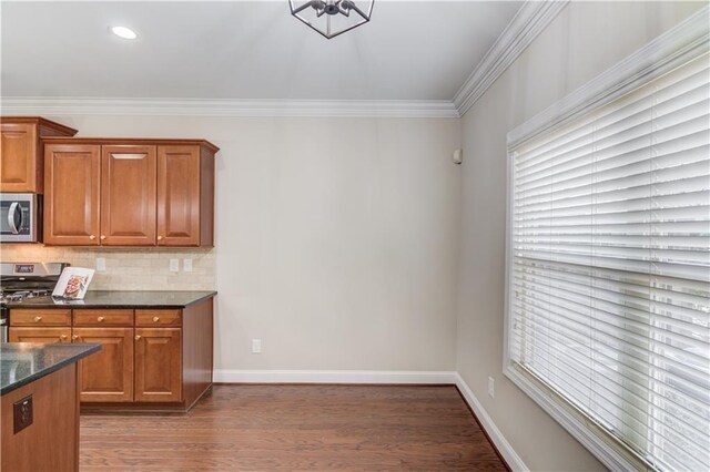 kitchen with wood finished floors, appliances with stainless steel finishes, brown cabinets, decorative backsplash, and crown molding