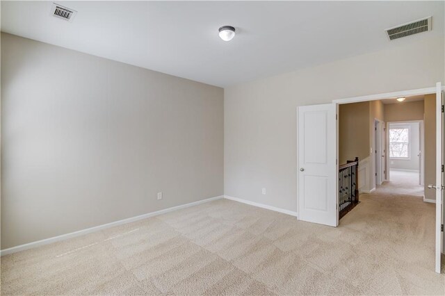 spare room featuring light colored carpet, visible vents, and baseboards