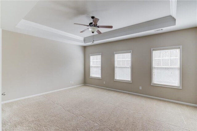 carpeted empty room featuring ornamental molding, a tray ceiling, visible vents, and baseboards