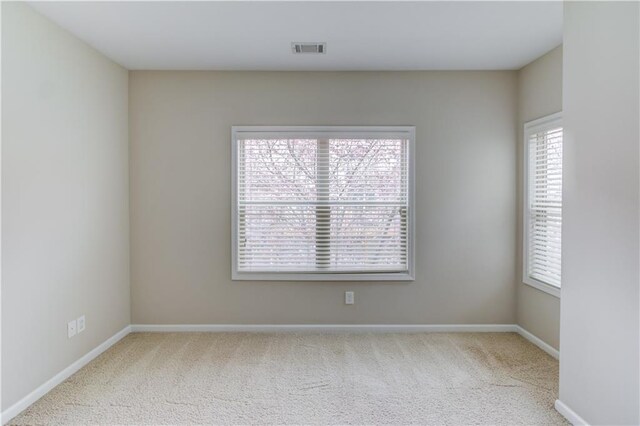 carpeted spare room with baseboards, visible vents, and a healthy amount of sunlight