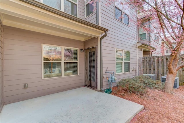 view of exterior entry with a patio, central AC unit, and fence