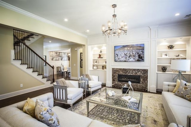 living room with built in shelves, a notable chandelier, wood-type flooring, a fireplace, and ornamental molding