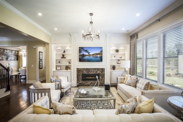 living room with built in features, a chandelier, wood-type flooring, a fireplace, and ornamental molding