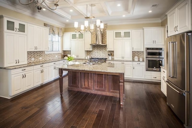 kitchen featuring white cabinets, hanging light fixtures, wall chimney exhaust hood, an island with sink, and appliances with stainless steel finishes