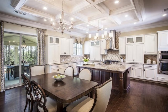 kitchen featuring wall chimney exhaust hood, dark wood-type flooring, an island with sink, pendant lighting, and white cabinets