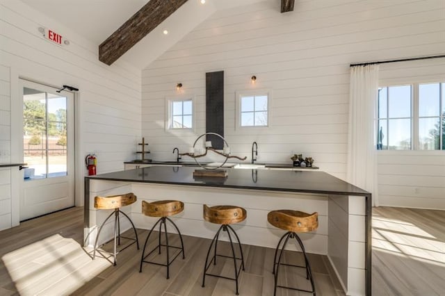 kitchen featuring a kitchen breakfast bar, light wood-type flooring, high vaulted ceiling, beamed ceiling, and wood walls