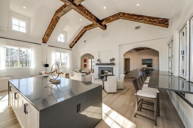 kitchen featuring beam ceiling, white cabinetry, high vaulted ceiling, a spacious island, and light hardwood / wood-style floors