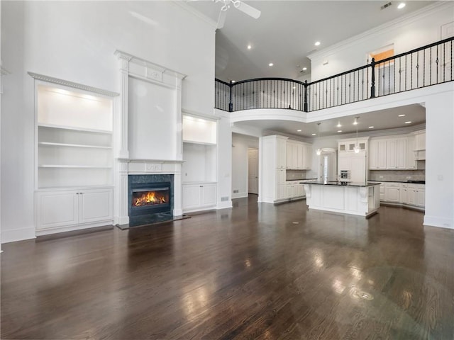 unfurnished living room with built in shelves, dark hardwood / wood-style floors, ceiling fan, a high end fireplace, and a high ceiling