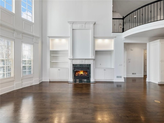 unfurnished living room with a towering ceiling, dark hardwood / wood-style floors, a high end fireplace, ornamental molding, and built in shelves