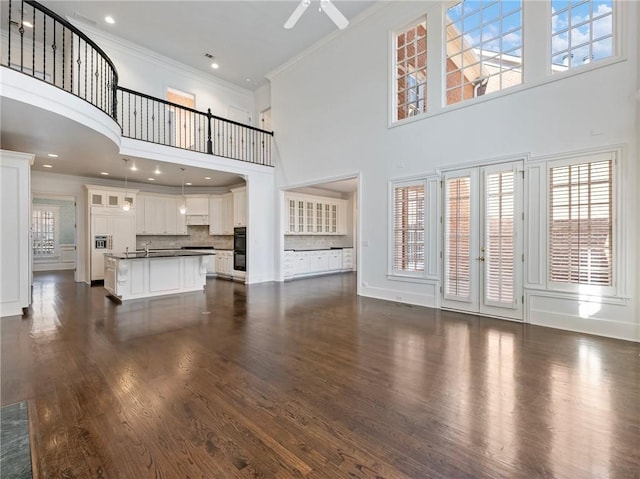 unfurnished living room featuring a towering ceiling, sink, ceiling fan, crown molding, and dark wood-type flooring