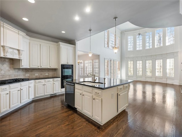 kitchen featuring sink, tasteful backsplash, decorative light fixtures, a towering ceiling, and a kitchen island with sink