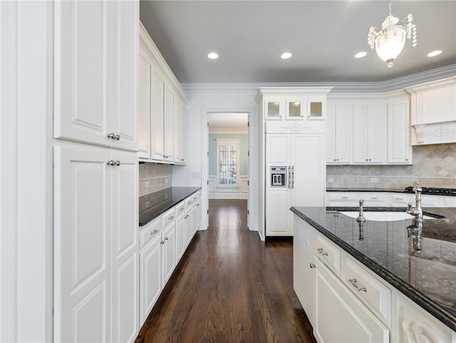 kitchen with hanging light fixtures, paneled refrigerator, ornamental molding, white cabinets, and dark stone counters