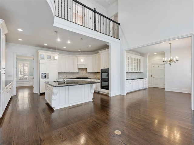 kitchen featuring tasteful backsplash, black double oven, white cabinetry, and a kitchen island with sink