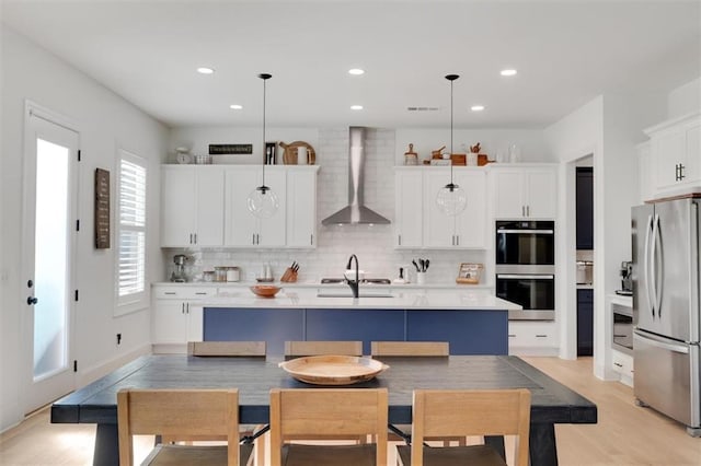 kitchen featuring wall chimney range hood, decorative backsplash, stainless steel appliances, and light countertops