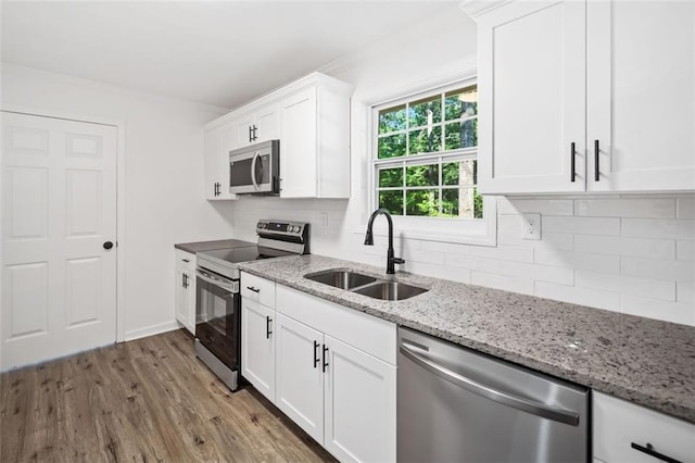 kitchen featuring appliances with stainless steel finishes, a sink, wood finished floors, tasteful backsplash, and white cabinetry