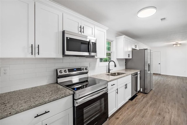 kitchen with stainless steel appliances, a sink, white cabinets, light wood finished floors, and light stone counters