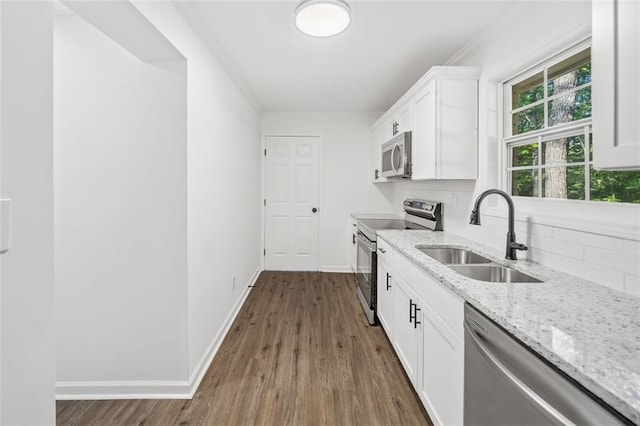 kitchen with stainless steel appliances, a sink, dark wood-type flooring, light stone counters, and decorative backsplash
