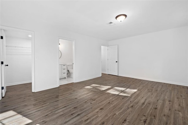 unfurnished bedroom featuring wood finished floors, a walk in closet, a closet, and baseboards