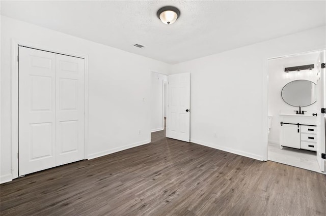 unfurnished bedroom featuring wood finished floors, a closet, baseboards, and connected bathroom