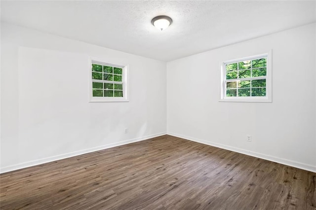 spare room with plenty of natural light, baseboards, and dark wood-type flooring