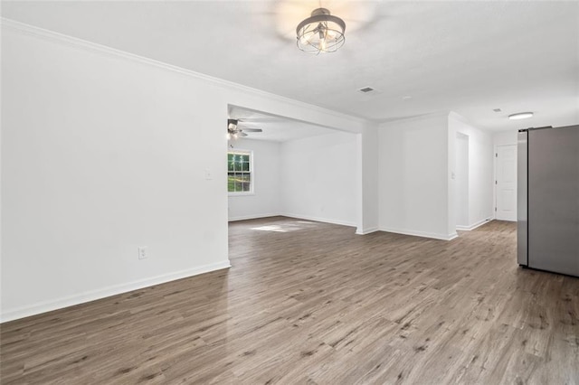 spare room featuring crown molding, a barn door, wood finished floors, baseboards, and ceiling fan