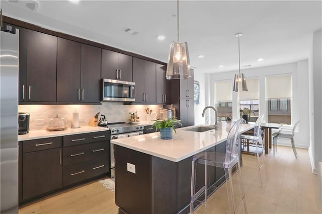 kitchen with sink, dark brown cabinets, stainless steel appliances, a center island with sink, and decorative light fixtures