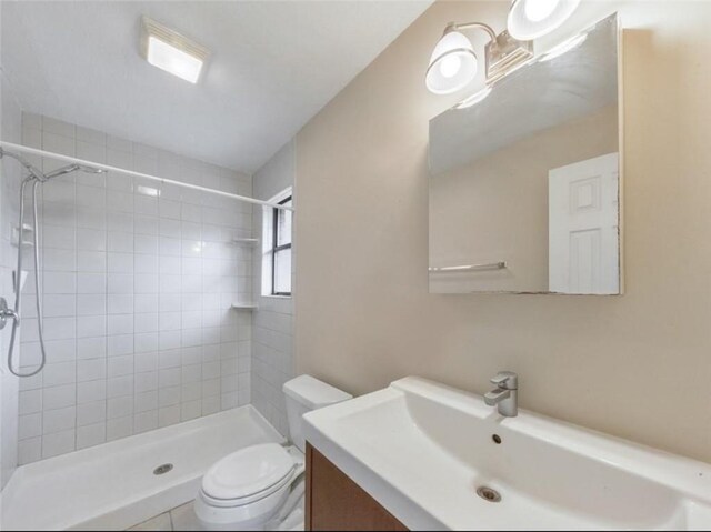 bathroom with tile patterned floors, tiled shower, vanity, and toilet