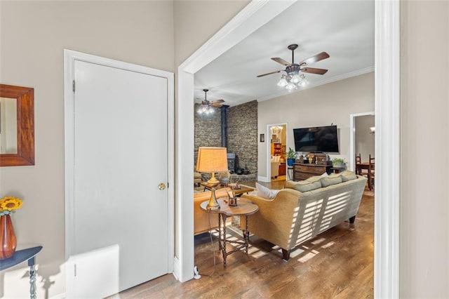 living room with a wood stove, ceiling fan, ornamental molding, and wood finished floors