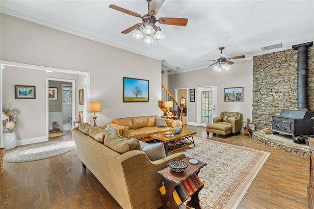 living area with crown molding, visible vents, a wood stove, wood finished floors, and stairs