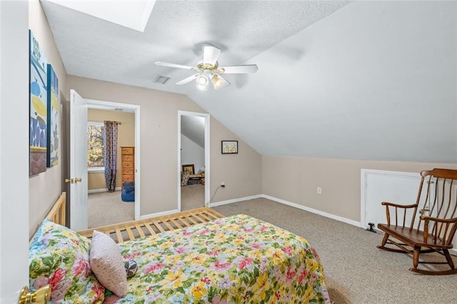 carpeted bedroom with visible vents, lofted ceiling with skylight, a ceiling fan, a textured ceiling, and baseboards