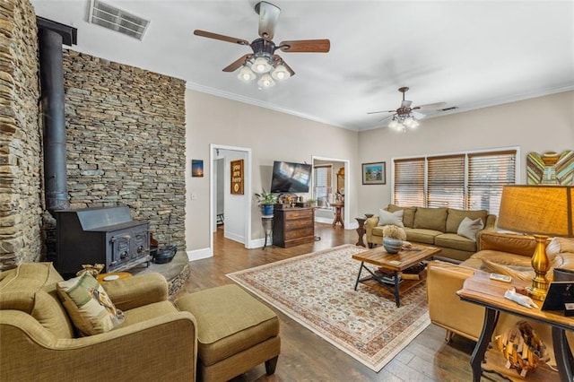 living area featuring visible vents, dark wood-type flooring, ornamental molding, a wood stove, and ceiling fan