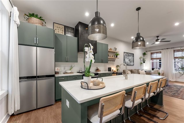 kitchen featuring stainless steel refrigerator, ceiling fan, light hardwood / wood-style flooring, a kitchen bar, and a center island with sink