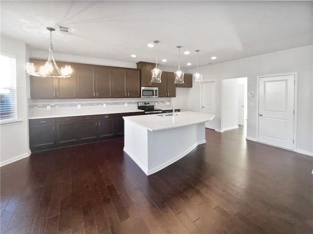 kitchen with a kitchen island with sink, sink, pendant lighting, dark wood-type flooring, and stainless steel appliances