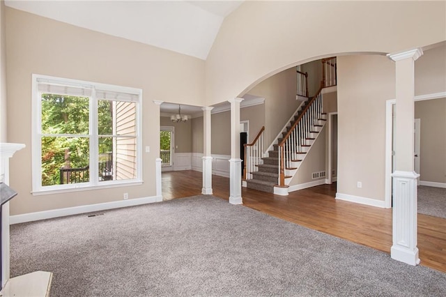 unfurnished living room featuring decorative columns, dark colored carpet, lofted ceiling, and an inviting chandelier