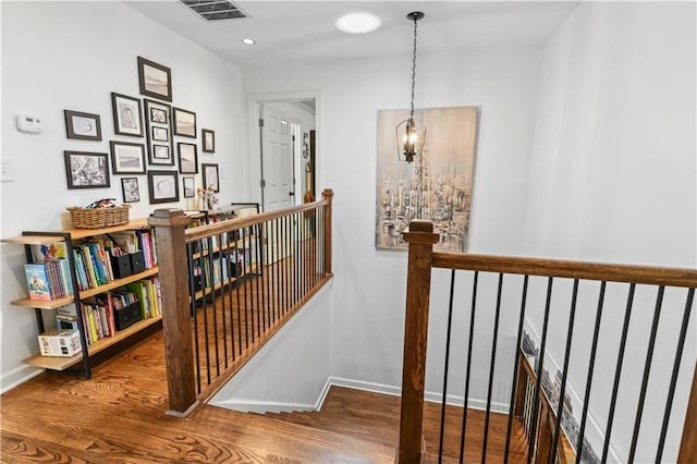 hall with baseboards, visible vents, an upstairs landing, and wood finished floors